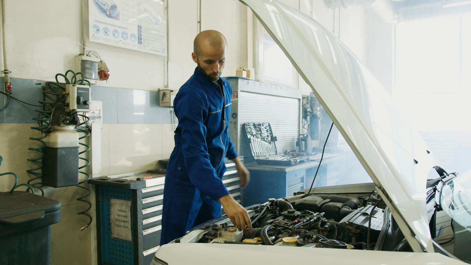 Mechanik w niebieskim kombinezonie sprawdza silnik Peugeota w warsztacie Mechanik w niebieskim kombinezonie sprawdza silnik Peugeota w warsztacie
