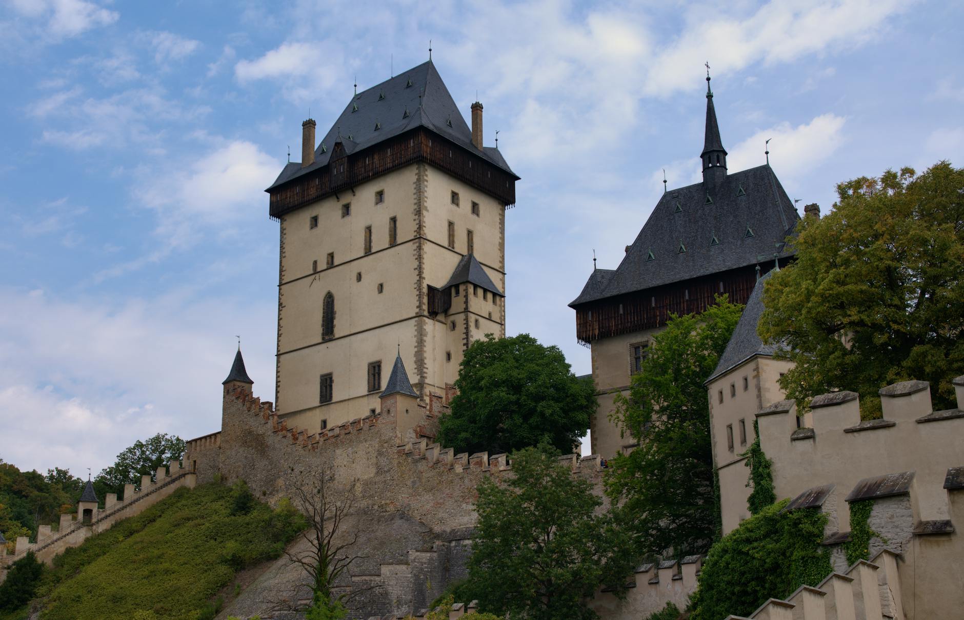 Zamek Karlštejn wśród zieleni pod pochmurnym niebem