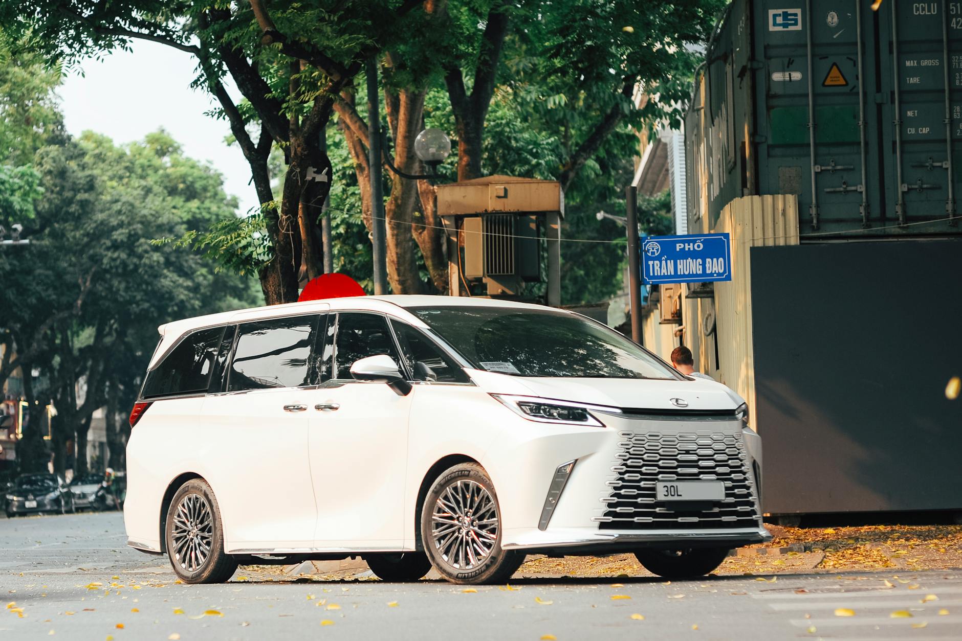 Biała Mazda 5 zaparkowana na rogu ulicy w otoczeniu drzew